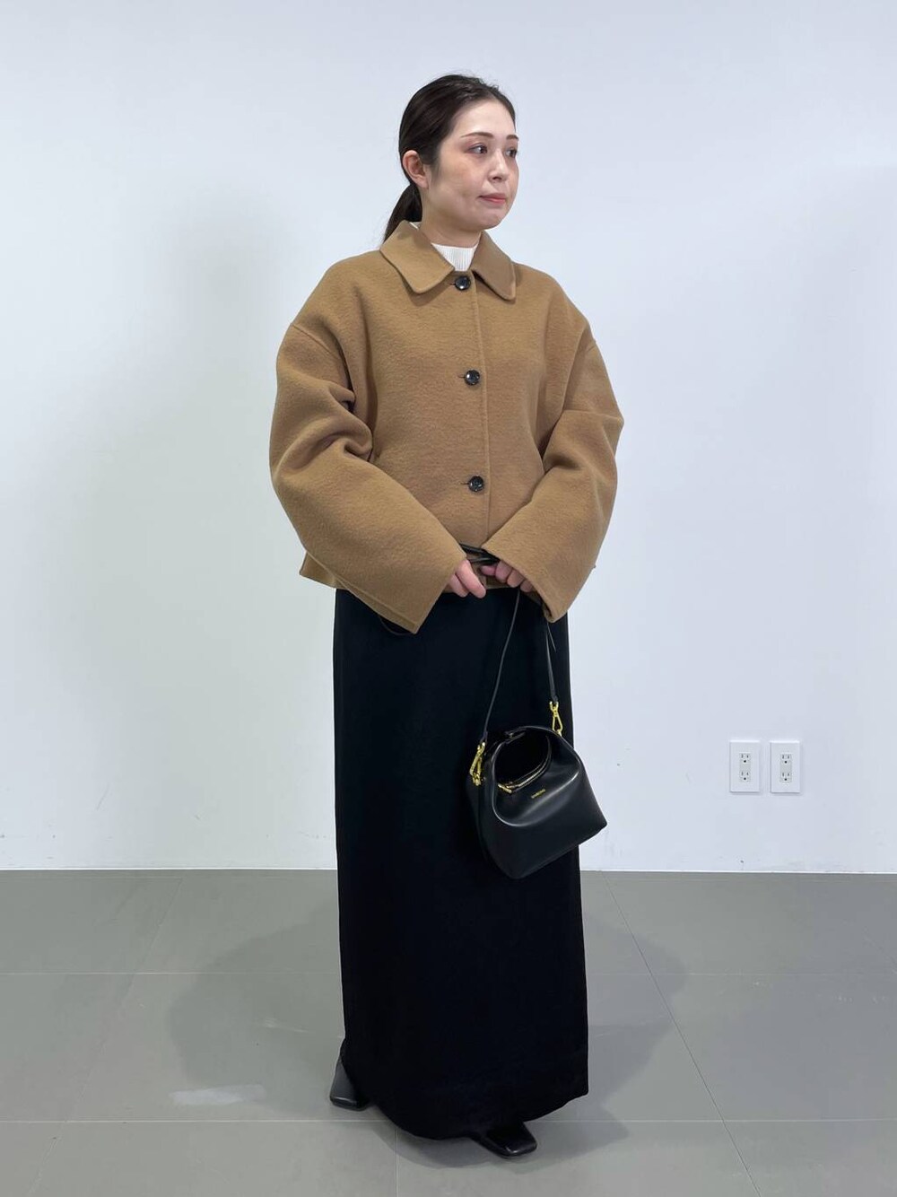 ブラック系のスカート、ベージュ系のその他アウター、ホワイト系のニット/セーターを着用したレディースの冬コーディネートの1枚目の写真