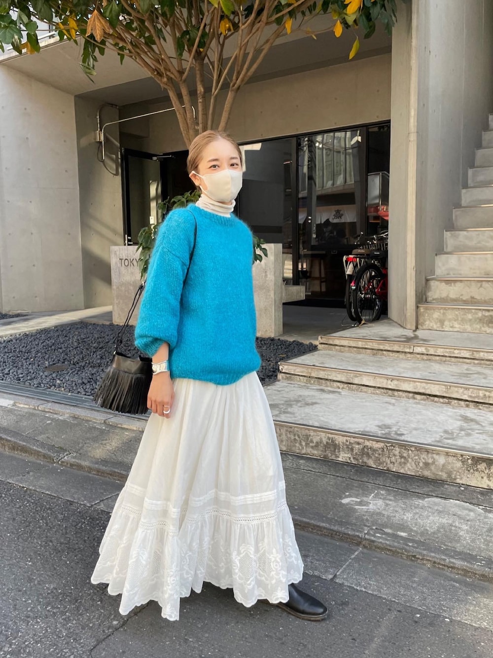 ブルー系のニット/セーター、ホワイト系のスカート、ブラック系のショルダーバッグを着用したレディースの冬コーディネートの1枚目の写真