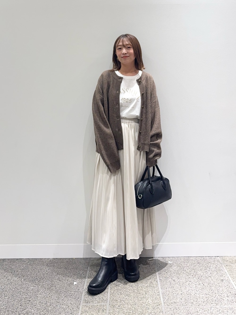ブラウン系のカーディガン/ボレロ、ホワイト系のスカート、ブラック系のショルダーバッグを着用したレディースの秋コーディネートの1枚目の写真