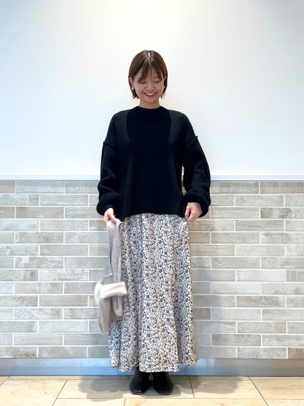 ブラック系のニット/セーター、ホワイト系のスカート、グレー系のハンドバッグを着用したレディースの秋コーディネートの1枚目の写真