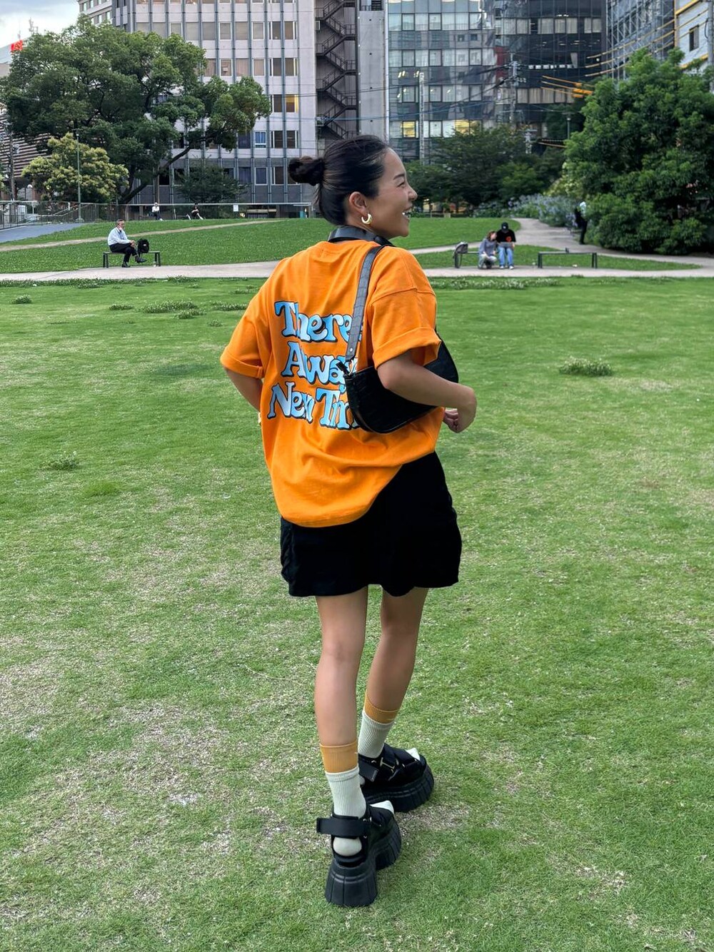 ブラック系のスニーカー、ブラック系のスカート、オレンジ系のTシャツ/カットソーを着用したレディースの夏コーディネートの1枚目の写真