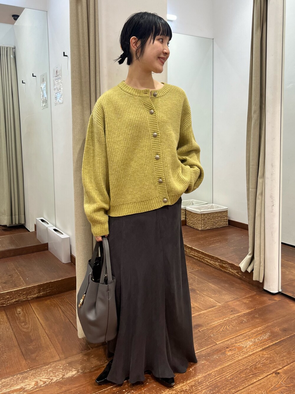 グレー系のトートバッグ、グレー系のスカート、ブラック系のパンプスを着用したレディースの秋コーディネートの1枚目の写真