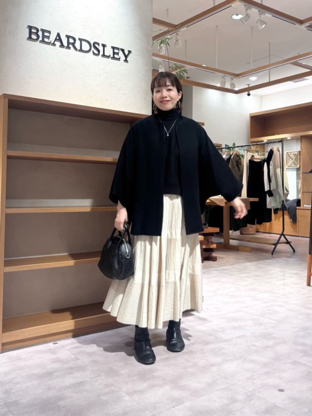 ホワイト系のスカート、ブラック系のその他アウター、ブラック系のボストンバッグを着用したレディースの冬コーディネートの1枚目の写真