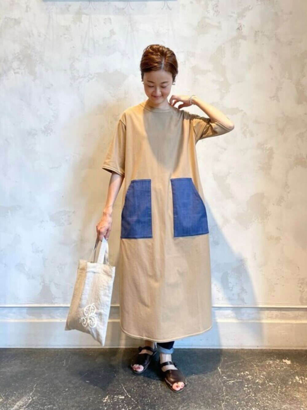 イエロー系のワンピース、ブルー系のデニムパンツ、ベージュ系のトートバッグを着用したレディースの夏コーディネートの1枚目の写真