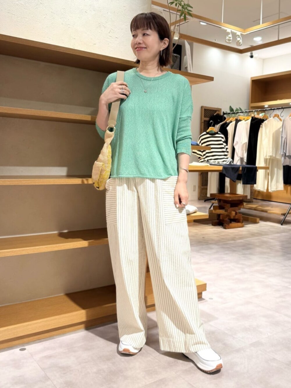 ベージュ系のその他パンツ、グリーン系のニット/セーター、ホワイト系のスニーカーを着用したレディースの夏コーディネートの1枚目の写真