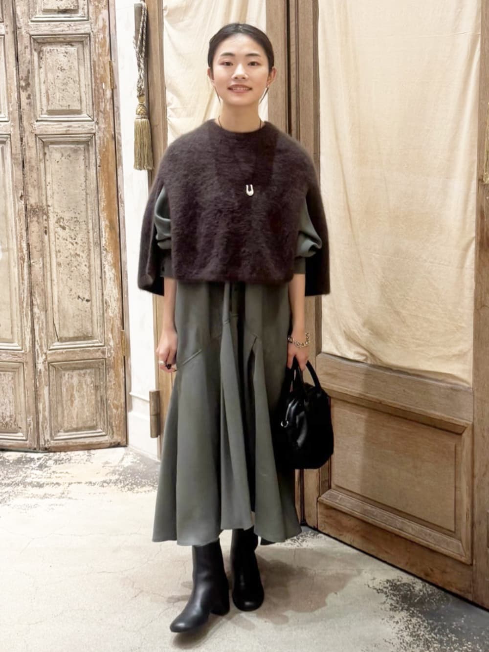 グリーン系のワンピース、ブラウン系のニット/セーター、ブラック系のボストンバッグを着用したレディースの秋コーディネートの1枚目の写真