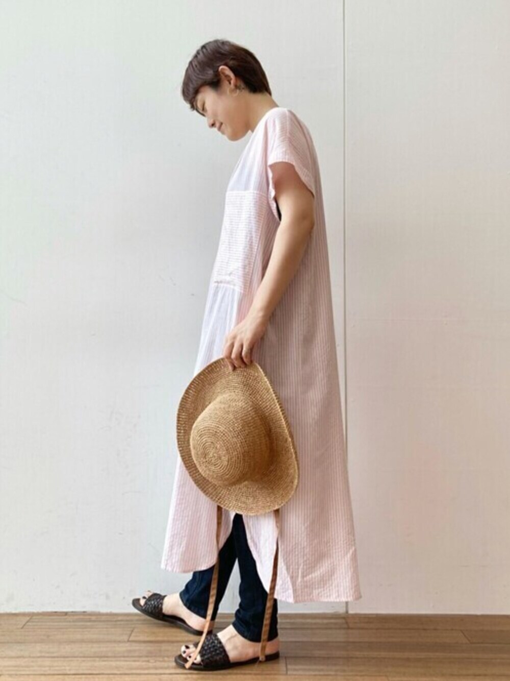 ピンク系のワンピース、ブルー系のデニムパンツ、ブラウン系のサンダルを着用したレディースの夏コーディネートの1枚目の写真