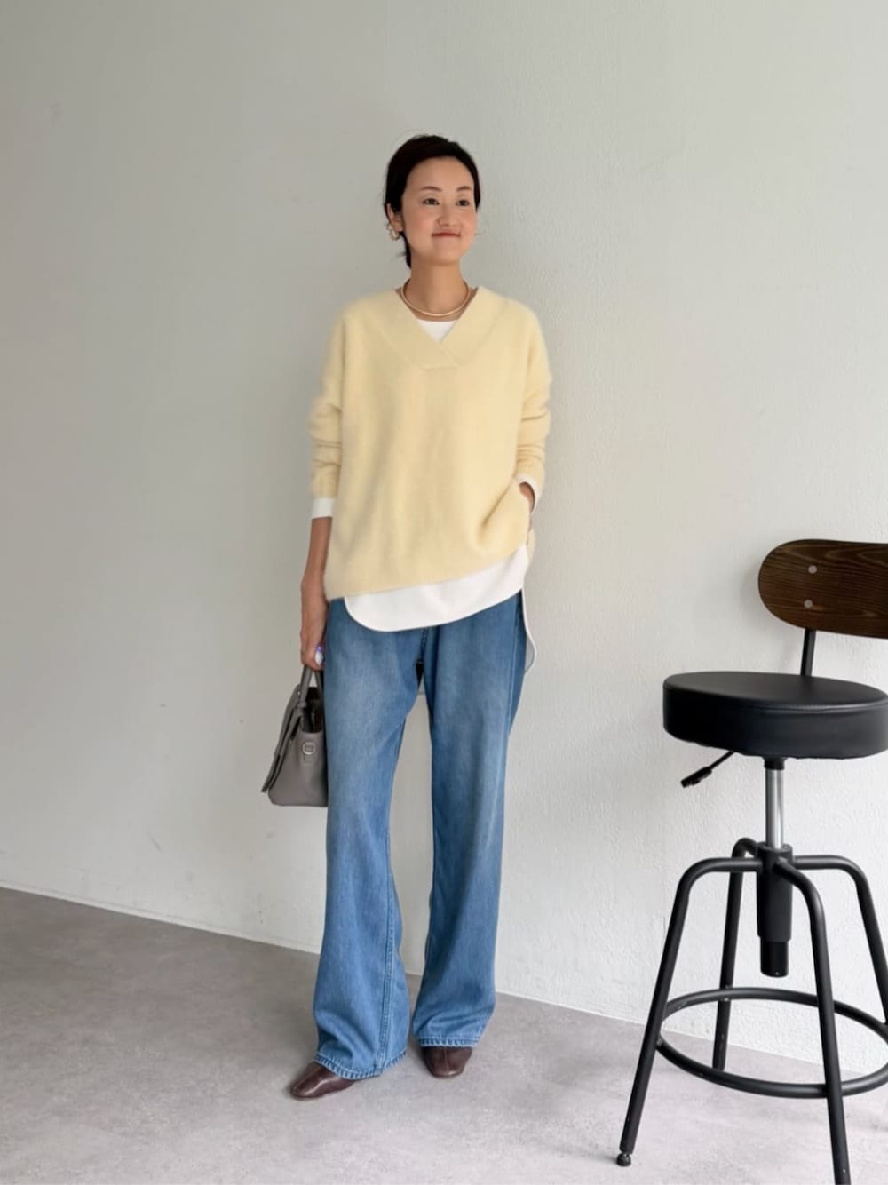 グレー系のハンドバッグ、ホワイト系のシャツ/ブラウス、イエロー系のニット/セーターを着用したレディースの秋コーディネートの1枚目の写真