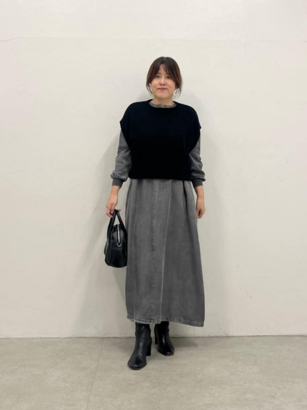 グレー系のワンピース、ブラック系のベストを着用したレディースの秋コーディネートの1枚目の写真