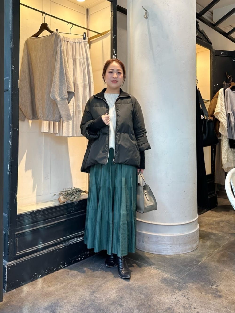 グリーン系のスカート、グレー系のニット/セーター、ブラック系のダウンジャケット/コートを着用したレディースの冬コーディネートの1枚目の写真