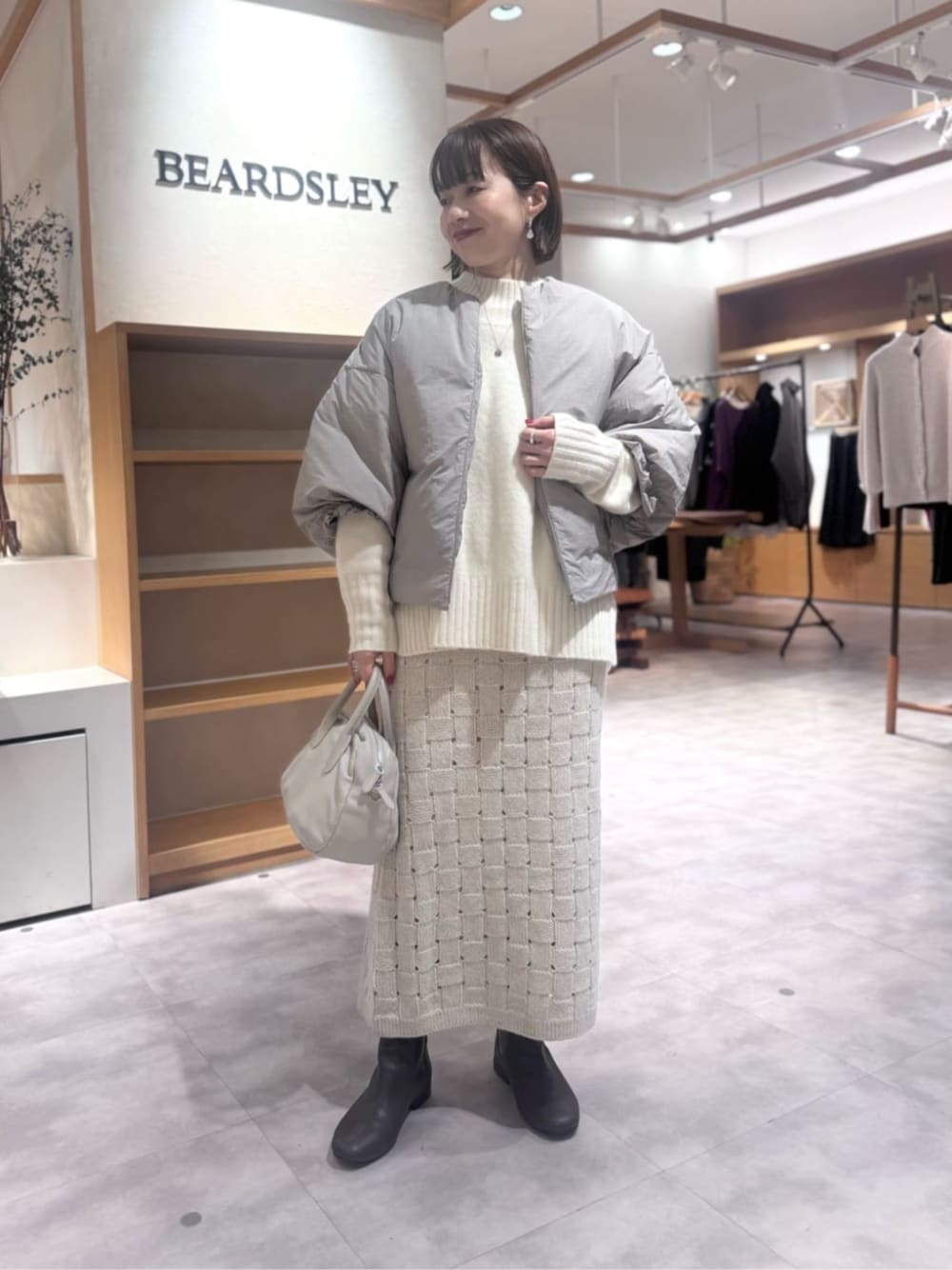 グレー系のボストンバッグ、ベージュ系のスカート、ブラウン系のダウンジャケット/コートを着用したレディースの冬コーディネートの1枚目の写真