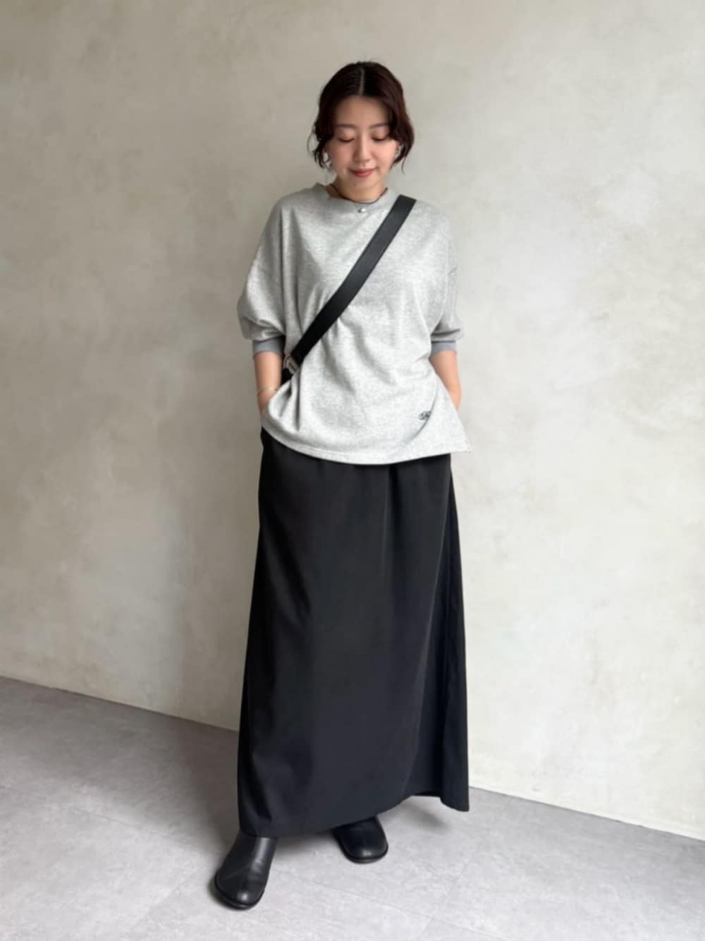 グレー系のTシャツ/カットソー、ブラック系のスカート、ブラック系のブーツを着用したレディースの秋コーディネートの1枚目の写真