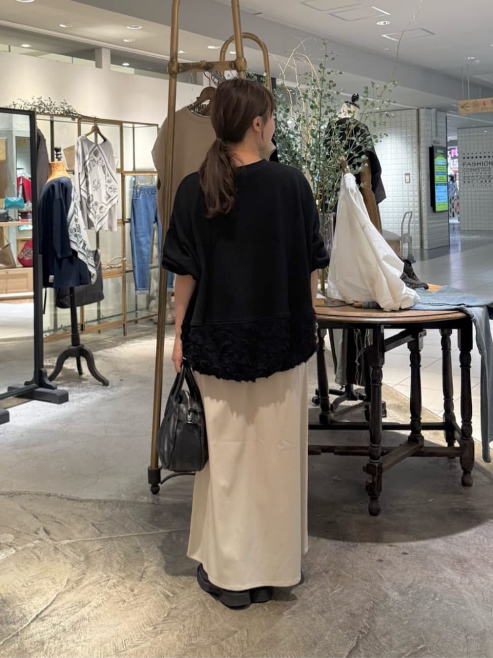 ブラック系のトートバッグ、ベージュ系のスカート、ブラック系のTシャツ/カットソーを着用したレディースの秋コーディネートの1枚目の写真