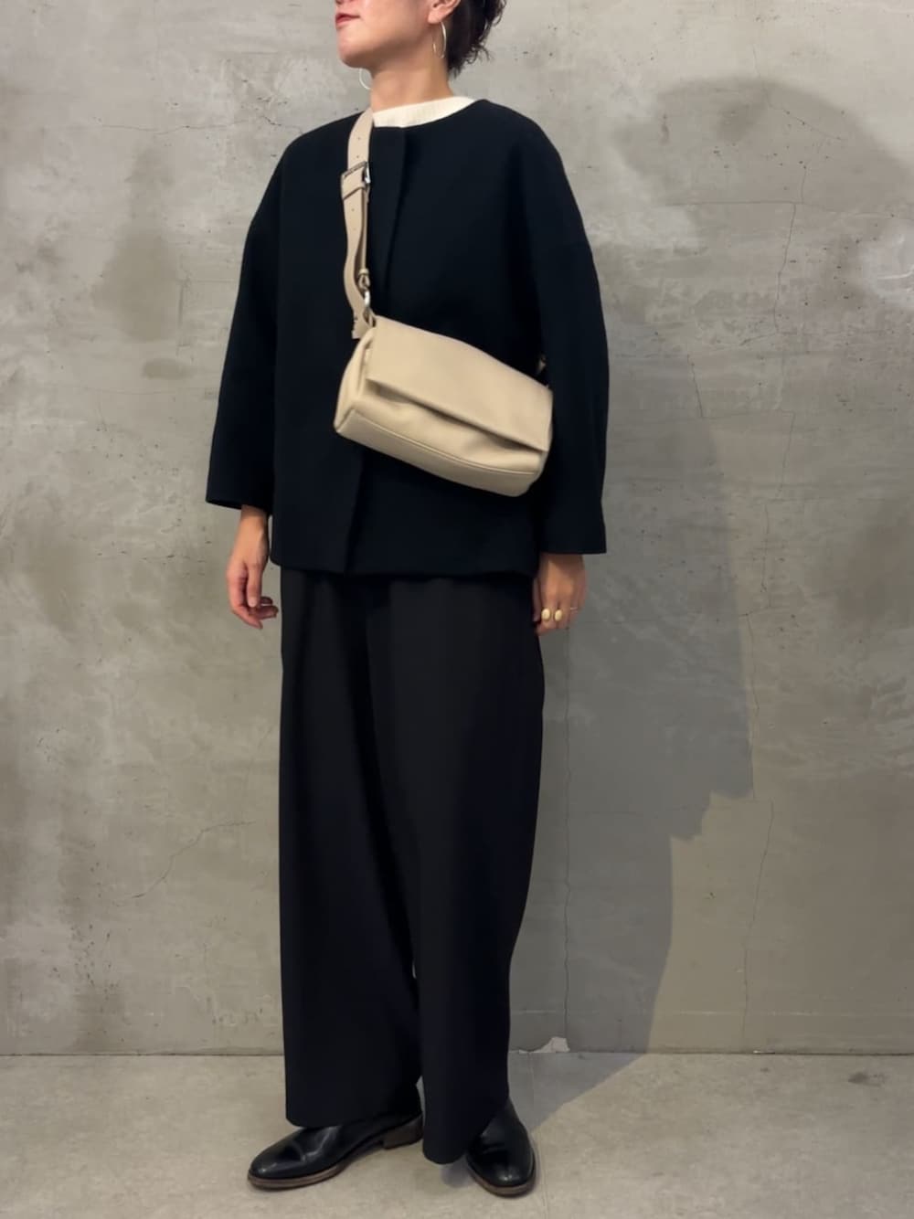 ブラック系のノーカラーコート、ブラック系のその他パンツ、ホワイト系のショルダーバッグを着用したレディースの冬コーディネートの1枚目の写真