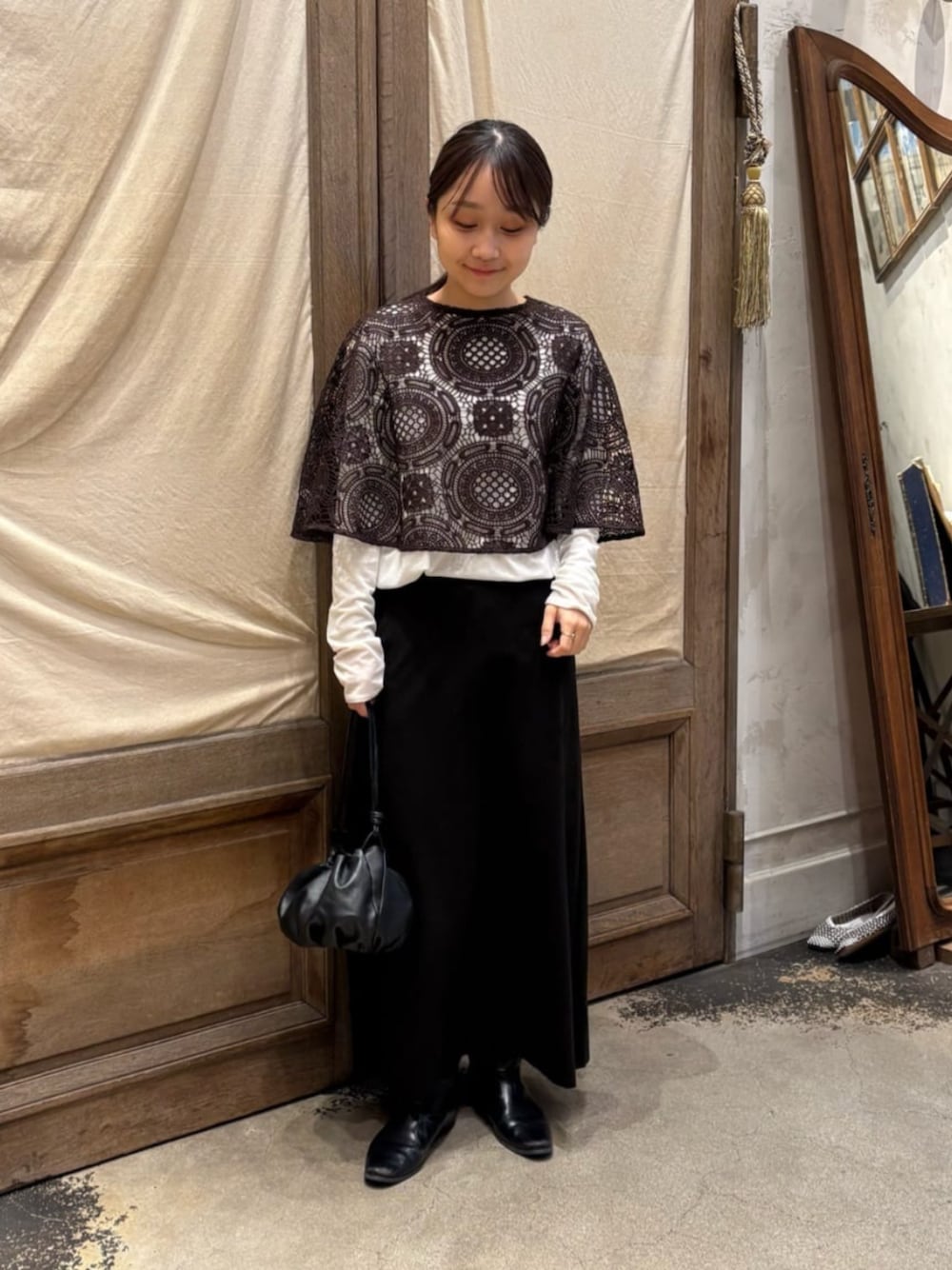 ブラック系のスカート、ホワイト系のTシャツ/カットソー、ブラウン系のポンチョを着用したレディースの冬コーディネートの1枚目の写真