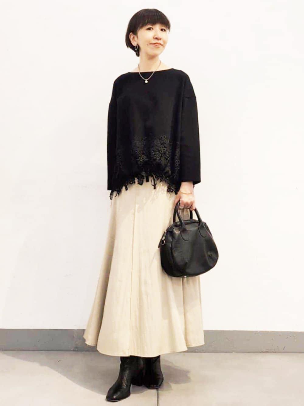 ブラック系のボストンバッグ、ベージュ系のスカート、ブラック系のニット/セーターを着用したレディースの夏コーディネートの1枚目の写真