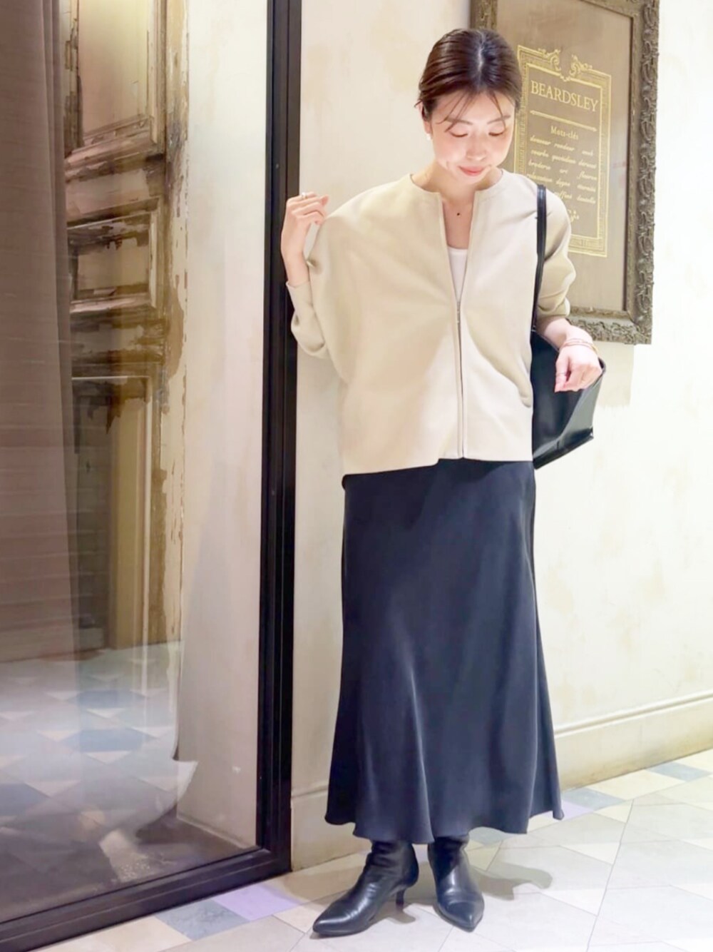 ブラック系のスカート、ブラック系のトートバッグ、ベージュ系のカーディガン/ボレロを着用したレディースの夏コーディネートの1枚目の写真