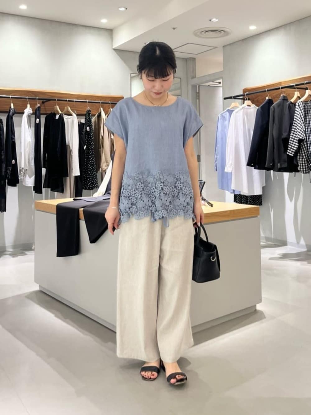 ブラック系のハンドバッグ、ベージュ系のその他パンツ、ブルー系のシャツ/ブラウスを着用したレディースの夏コーディネートの1枚目の写真