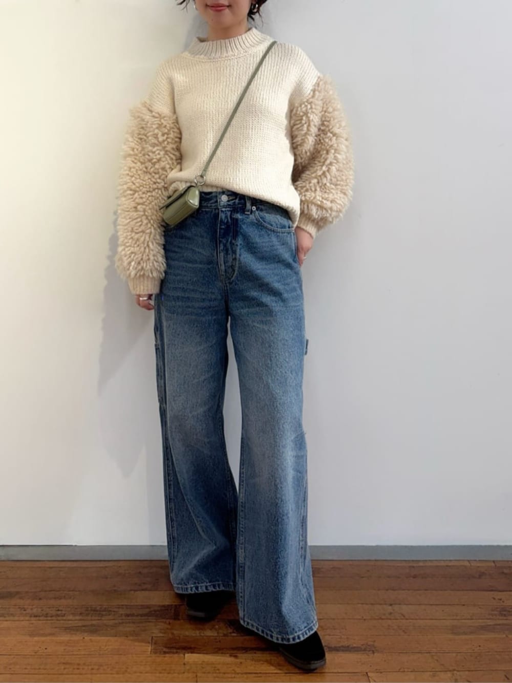 ブルー系のデニムパンツ、ホワイト系のニット/セーター、グリーン系のポーチを着用したレディースの秋コーディネートの1枚目の写真