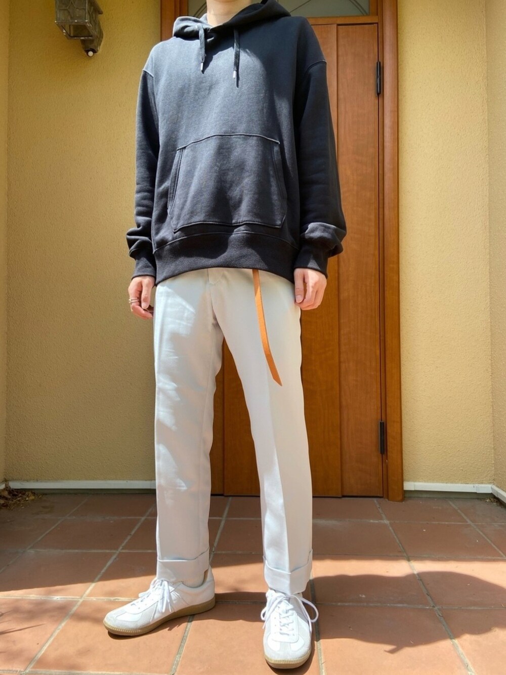 ブラック系のパーカー、ホワイト系のスラックス、ホワイト系のスニーカーを着用したメンズの春コーディネートの1枚目の写真