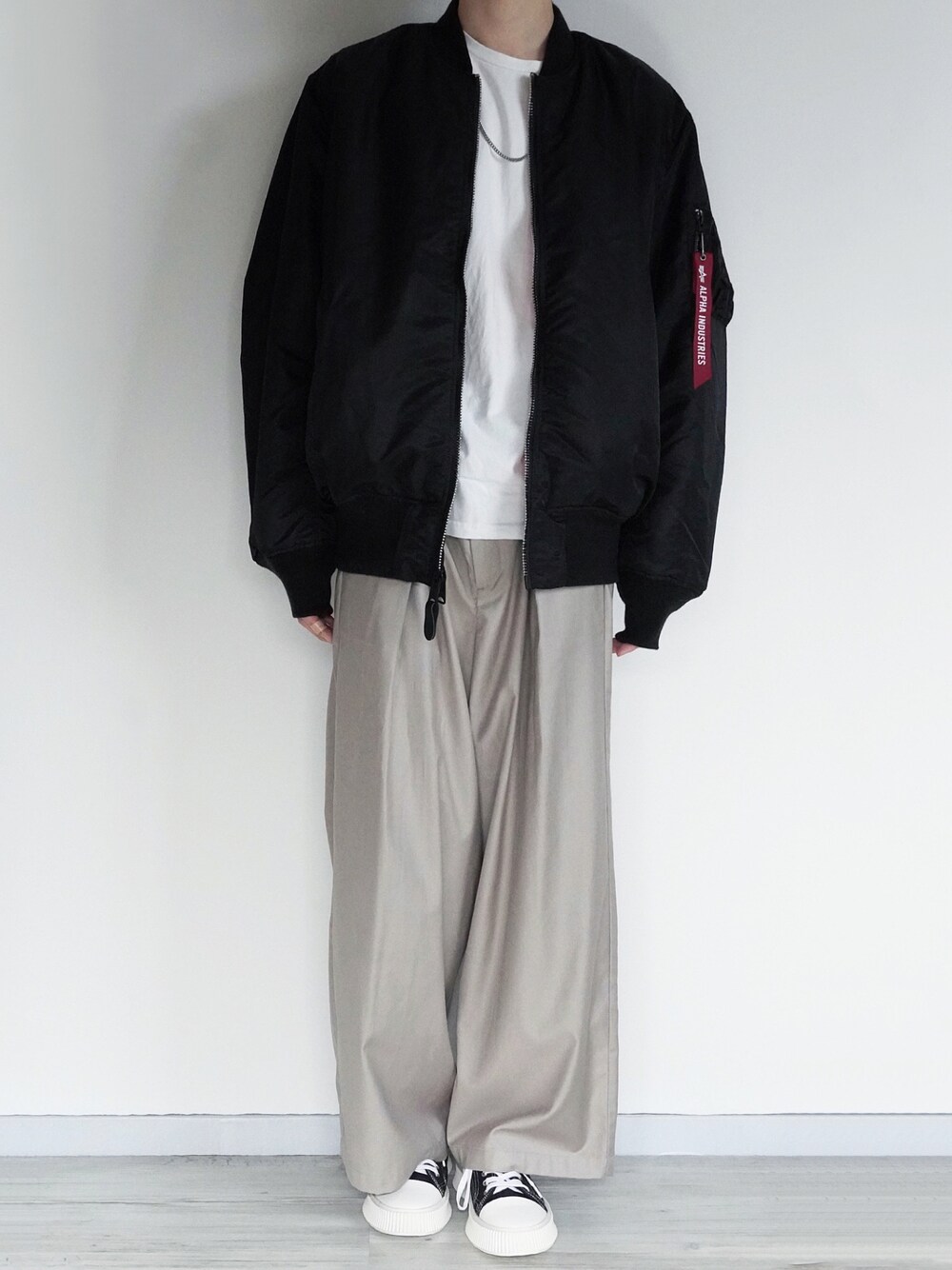 ブラック系のMA-1、ホワイト系のTシャツ/カットソー、ベージュ系のスラックスを着用したメンズの冬コーディネートの1枚目の写真