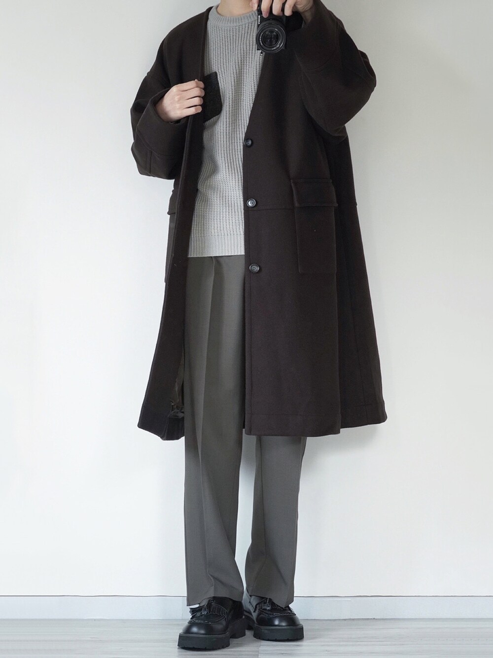 ブラウン系のノーカラーコート、グレー系のニット/セーター、ブラウン系のスラックスを着用したメンズの冬コーディネートの1枚目の写真