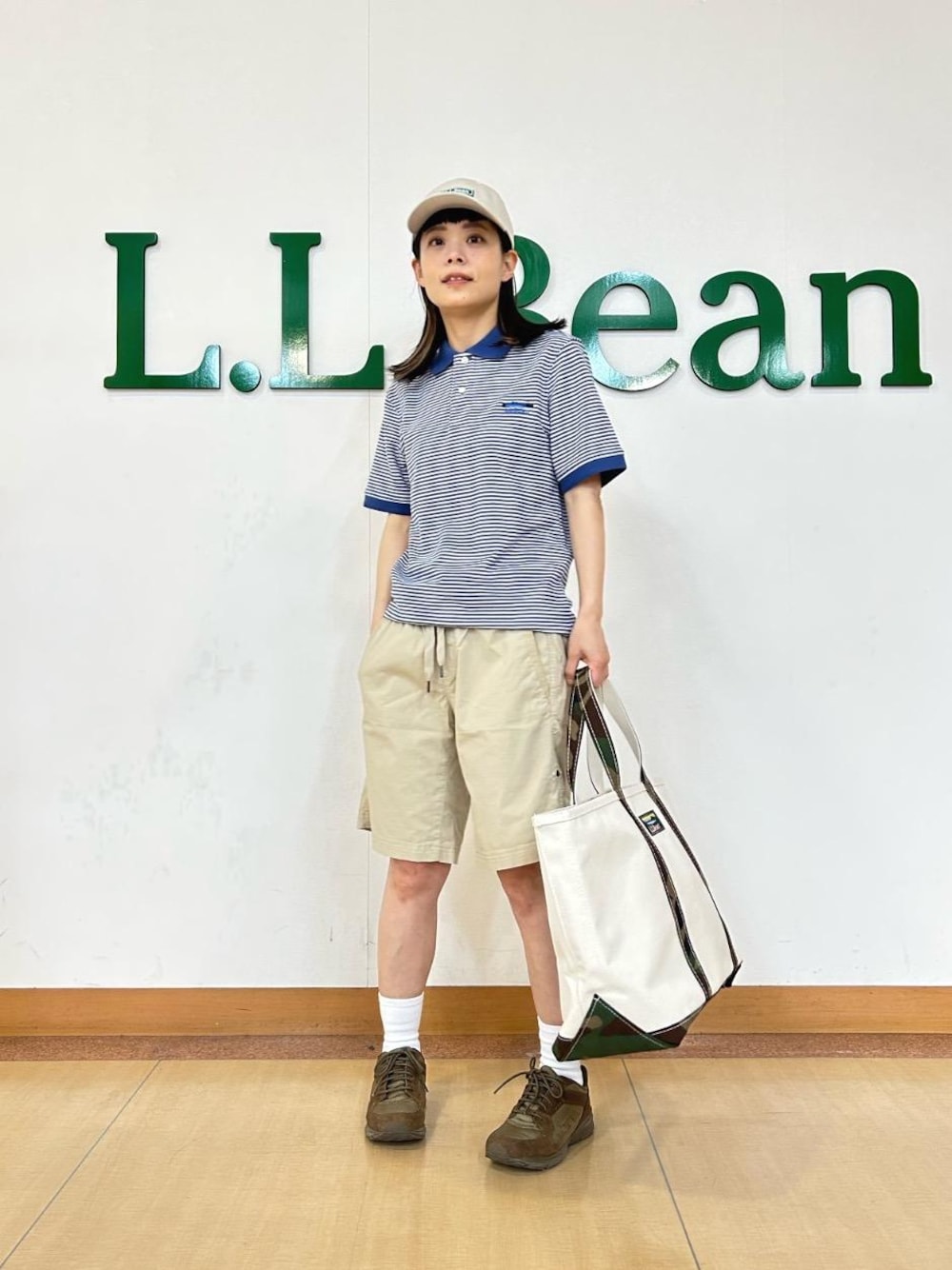 ホワイト系のトートバッグ、ブルー系のポロシャツ、ベージュ系のキャップを着用したレディースの夏コーディネートの1枚目の写真