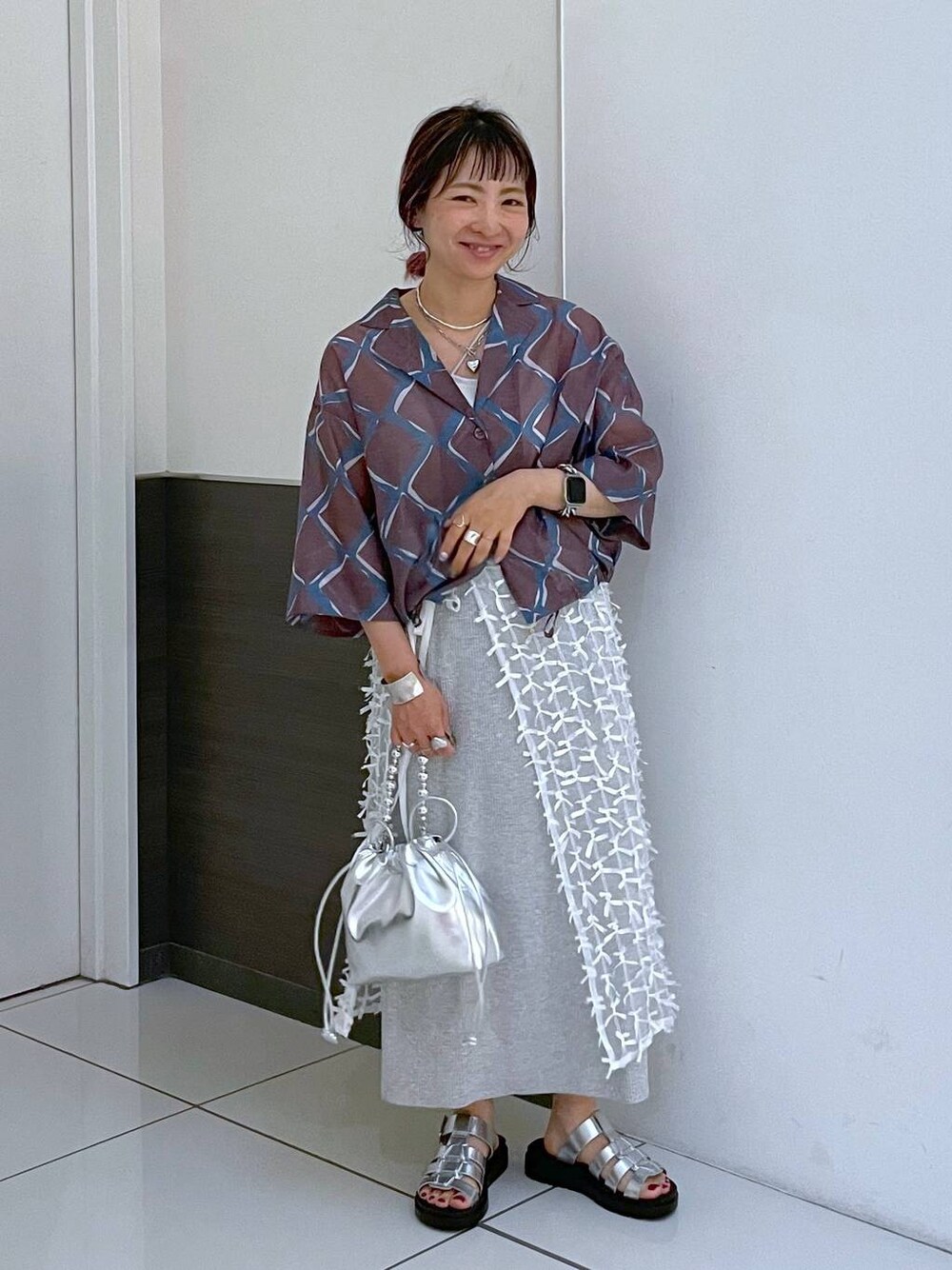 グレー系のスカート、シルバー系のスニーカー、シルバー系のショルダーバッグを着用したレディースの夏コーディネートの1枚目の写真