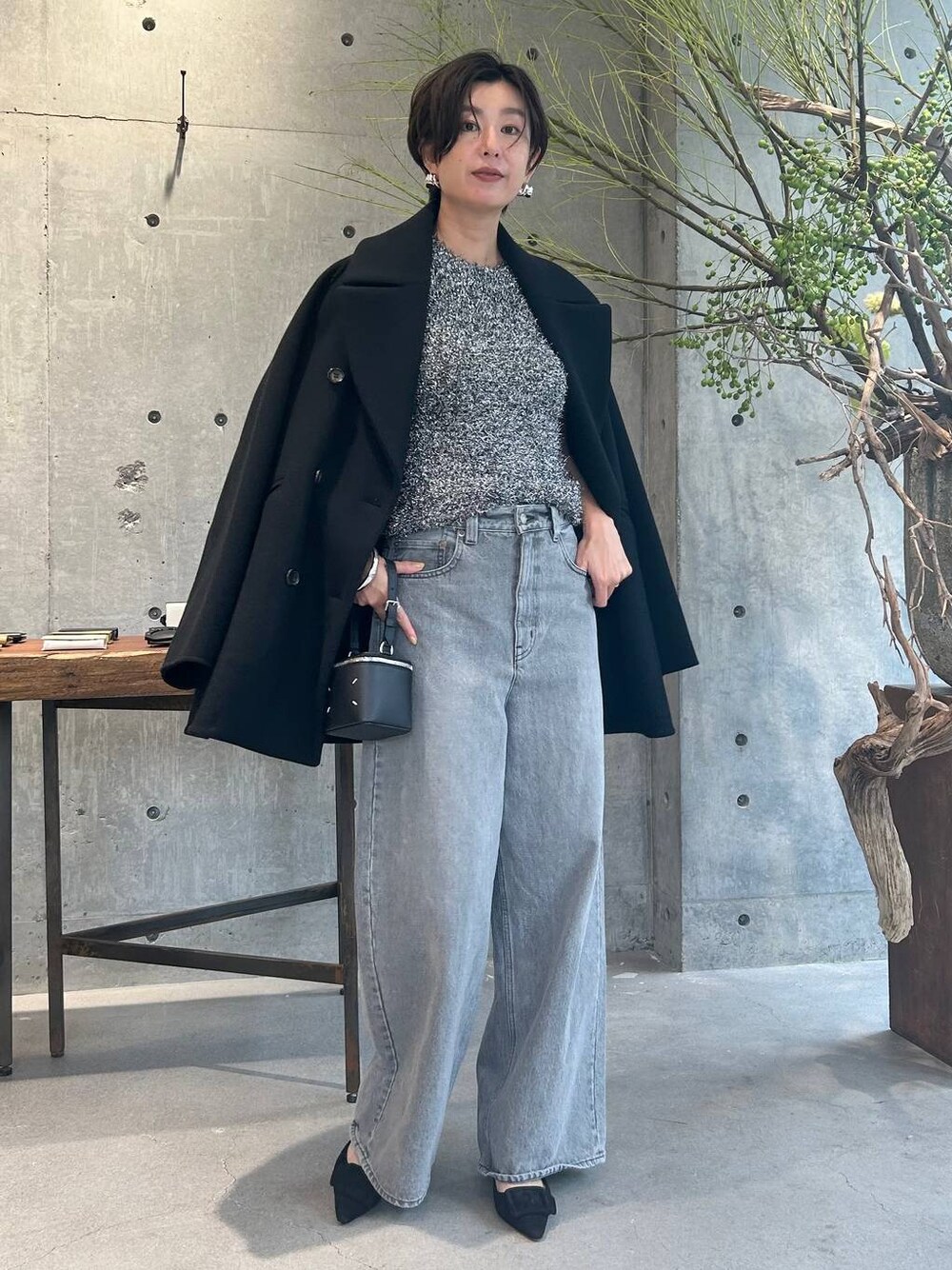 グレー系のデニムパンツ、ブラック系のピーコート、シルバー系のニット/セーターを着用したレディースの秋コーディネートの1枚目の写真