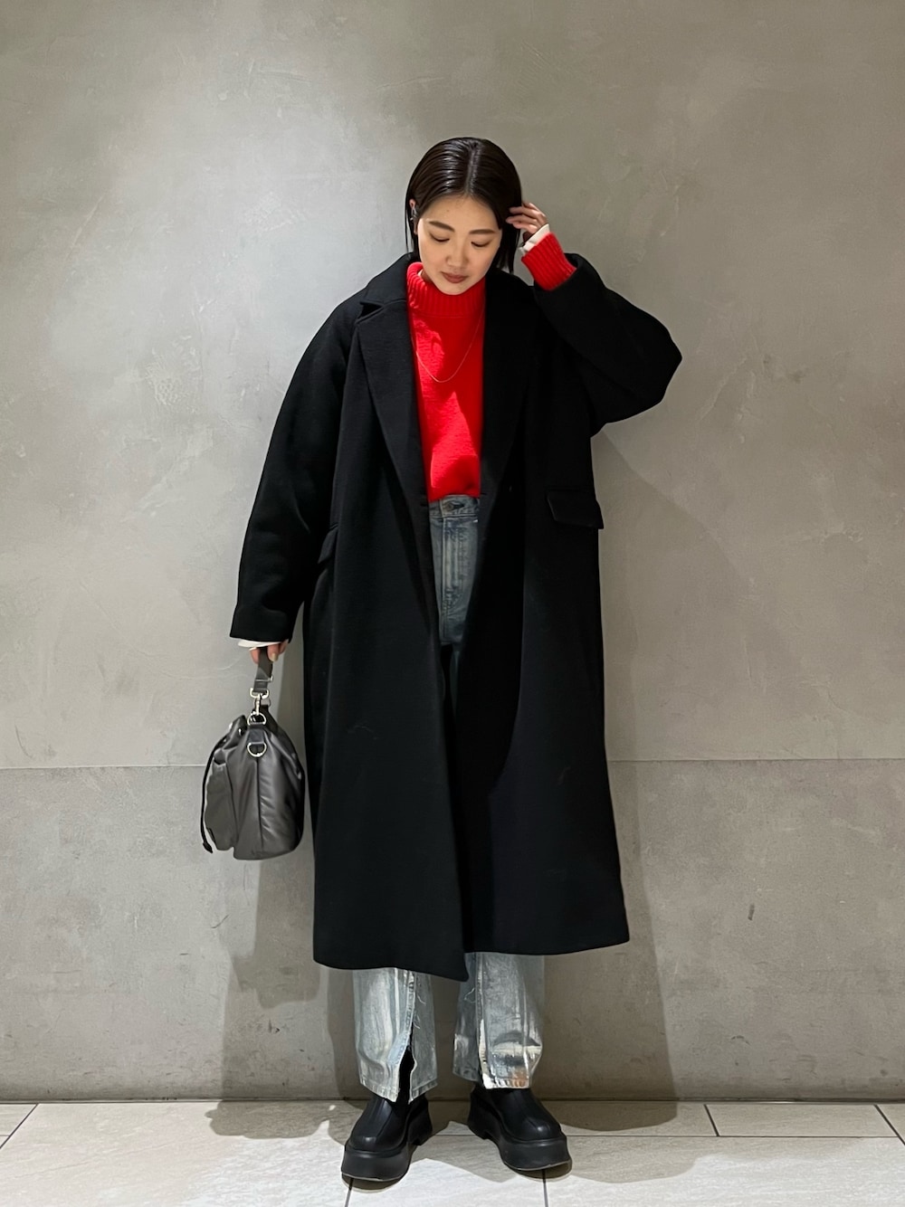 レッド系のニット/セーター、ブラック系のチェスターコート、ブルー系のデニムパンツを着用したレディースの冬コーディネートの1枚目の写真