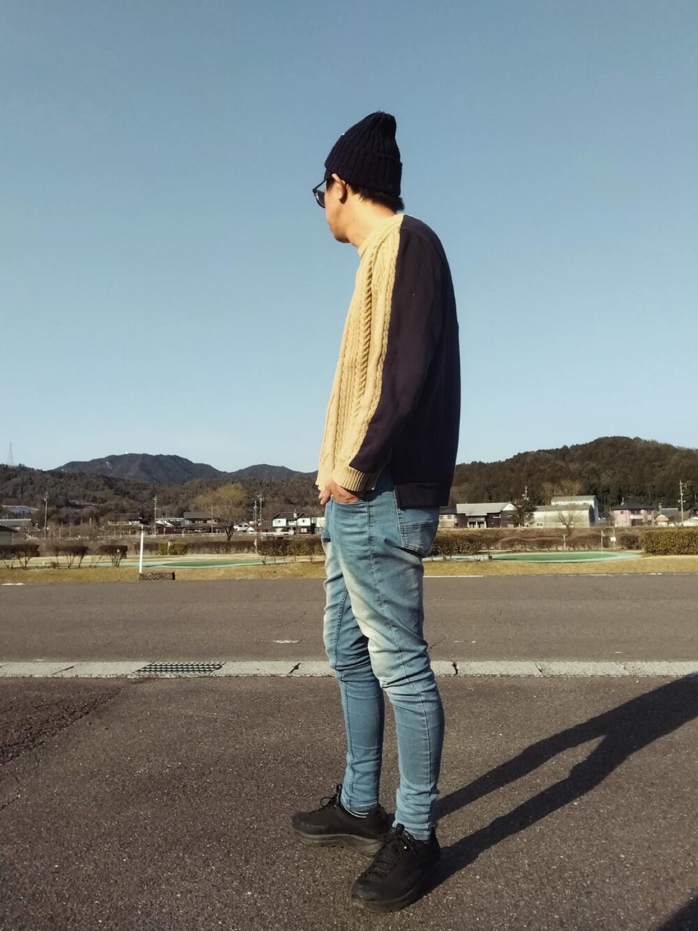 ブルー系のデニムパンツ、ブラック系のスニーカー、ベージュ系のニット/セーターを着用したメンズの春コーディネートの1枚目の写真