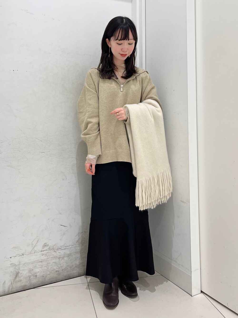 ブラウン系のブーツ、ベージュ系のニット/セーター、ブラック系のスカートを着用したレディースの冬コーディネートの1枚目の写真