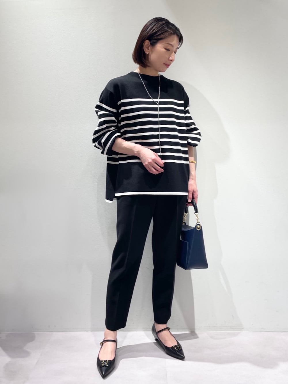 ブラック系のスラックス、ブルー系のハンドバッグ、ブラック系のパンプスを着用したレディースの冬コーディネートの1枚目の写真