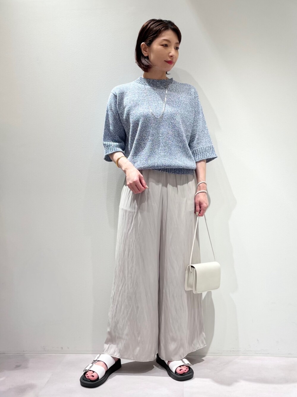 ブルー系のニット/セーター、グレー系のその他パンツ、ホワイト系のパンプスを着用したレディースの夏コーディネートの1枚目の写真