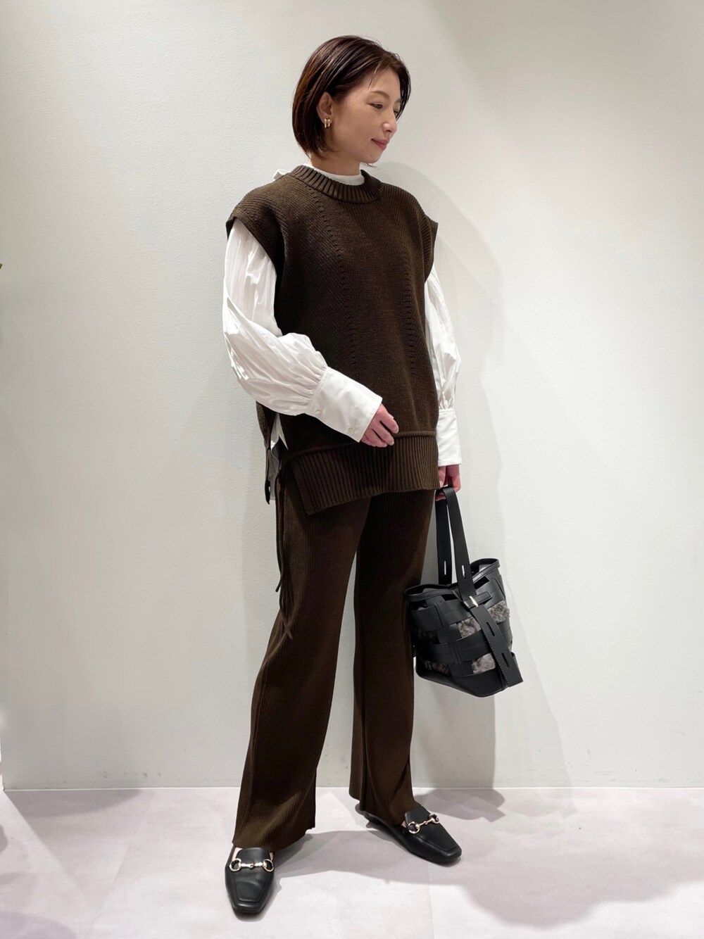 ブラウン系のベスト、ブラウン系のその他パンツ、ブラック系のハンドバッグを着用したレディースの秋コーディネートの1枚目の写真