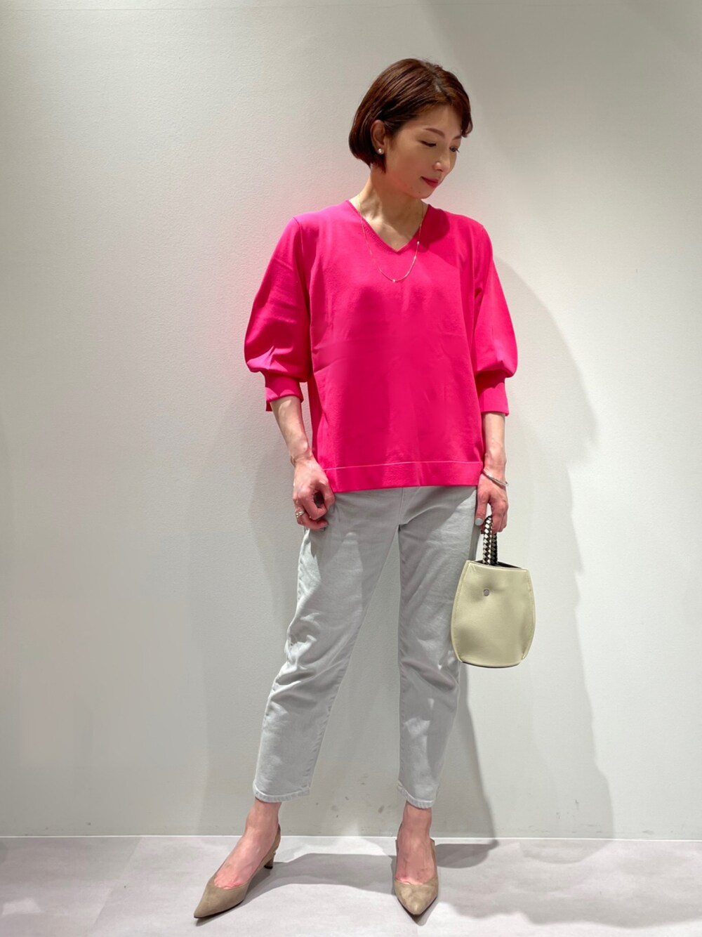 ピンク系のニット/セーター、グレー系のデニムパンツ、ホワイト系のショルダーバッグを着用したレディースの春コーディネートの1枚目の写真