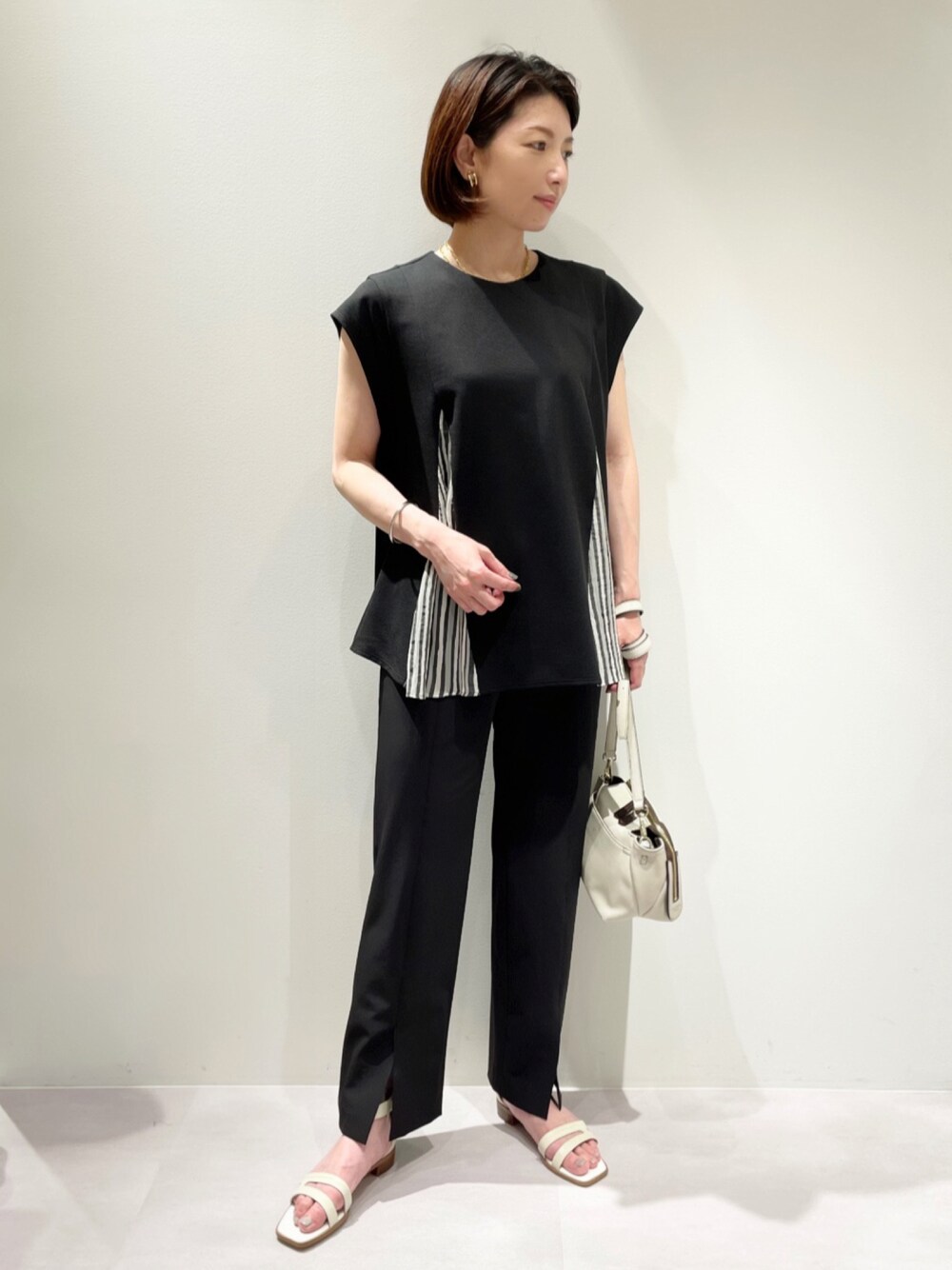 ブラック系のスラックス、ブラック系のTシャツ/カットソー、ホワイト系のショルダーバッグを着用したレディースの夏コーディネートの1枚目の写真