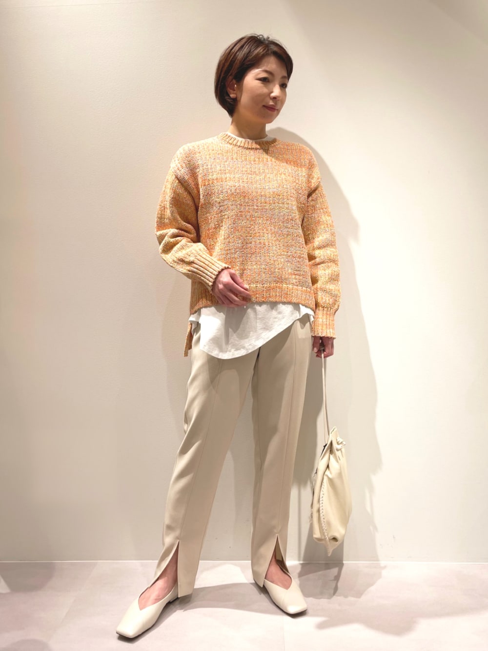 オレンジ系のニット/セーター、ベージュ系のその他パンツ、ホワイト系のパンプスを着用したレディースの冬コーディネートの1枚目の写真