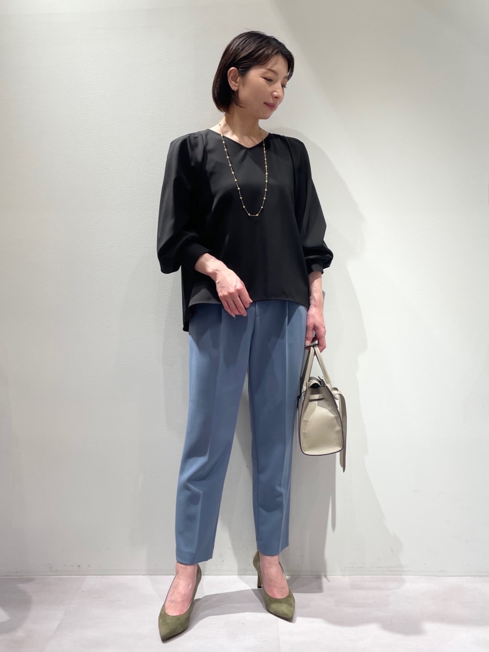 ブラック系のシャツ/ブラウス、ブルー系のスラックス、グリーン系のパンプスを着用したレディースの冬コーディネートの1枚目の写真