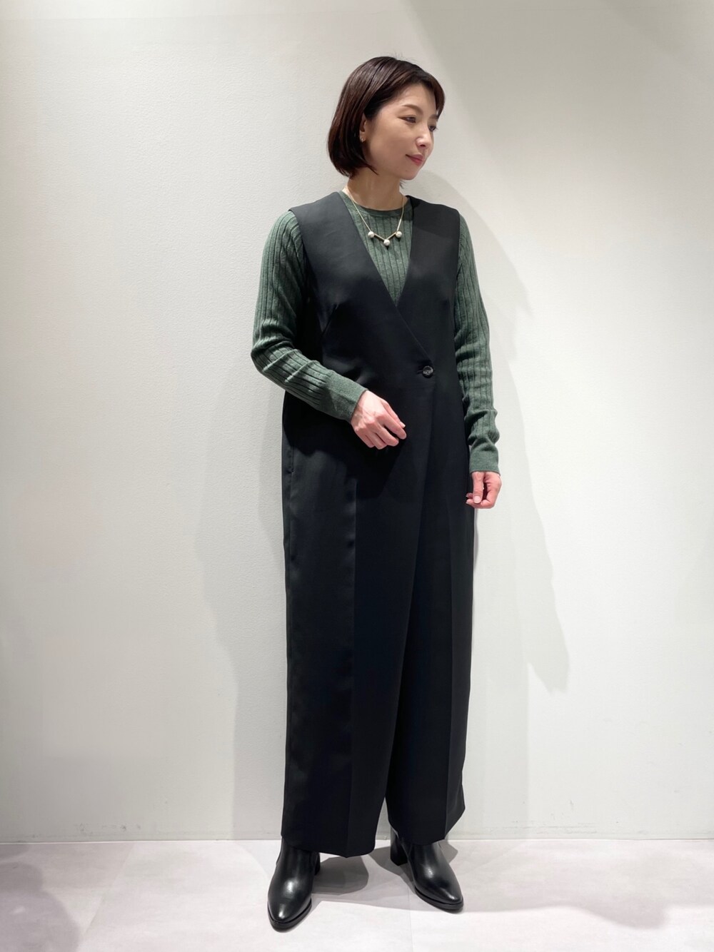 ブラック系のつなぎ/オールインワン、グリーン系のニット/セーター、ブラック系のブーツを着用したレディースの冬コーディネートの1枚目の写真