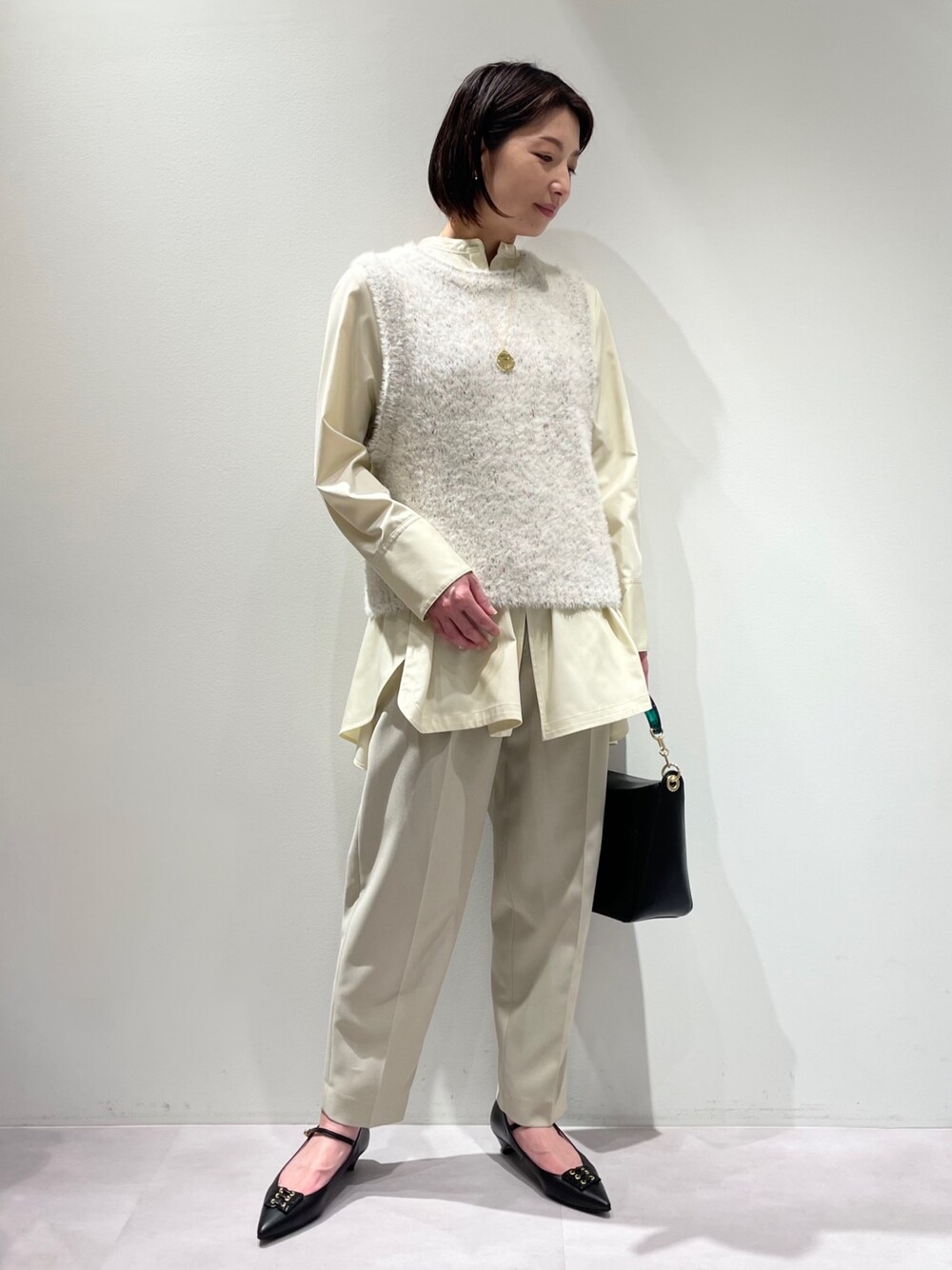 ベージュ系のスラックス、ホワイト系のニット/セーター、イエロー系のシャツ/ブラウスを着用したレディースの冬コーディネートの1枚目の写真