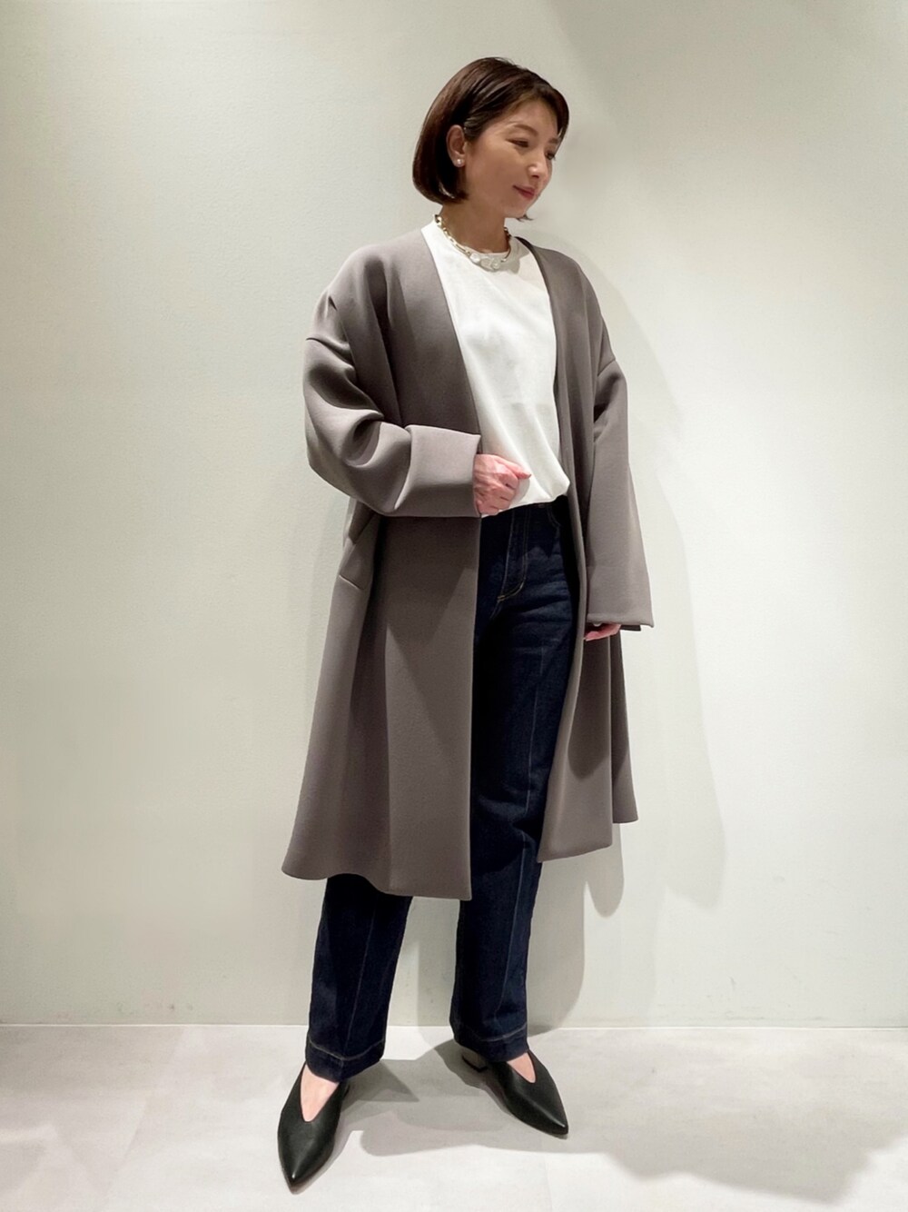 ベージュ系のノーカラーコート、ホワイト系のニット/セーター、ブルー系のデニムパンツを着用したレディースの冬コーディネートの1枚目の写真