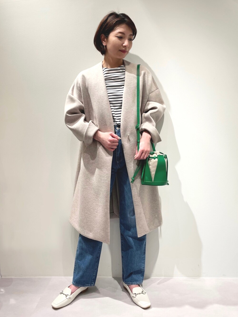 ベージュ系のノーカラーコート、ブルー系のデニムパンツ、ホワイト系のローファーを着用したレディースの春コーディネートの1枚目の写真