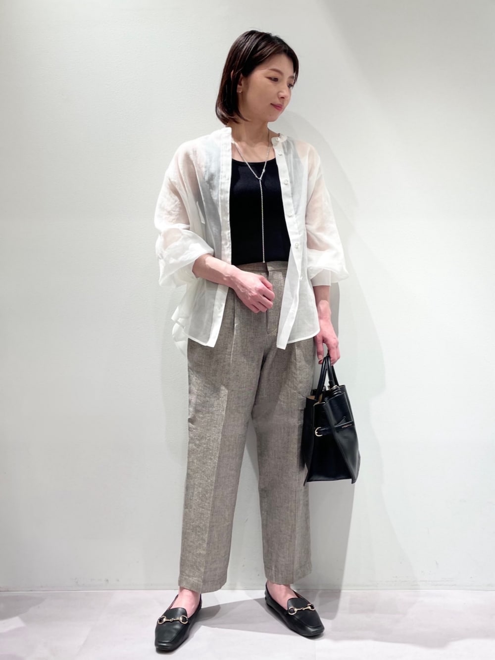 グレー系のスラックス、ホワイト系のシャツ/ブラウス、ブラック系のハンドバッグを着用したレディースの春コーディネートの1枚目の写真
