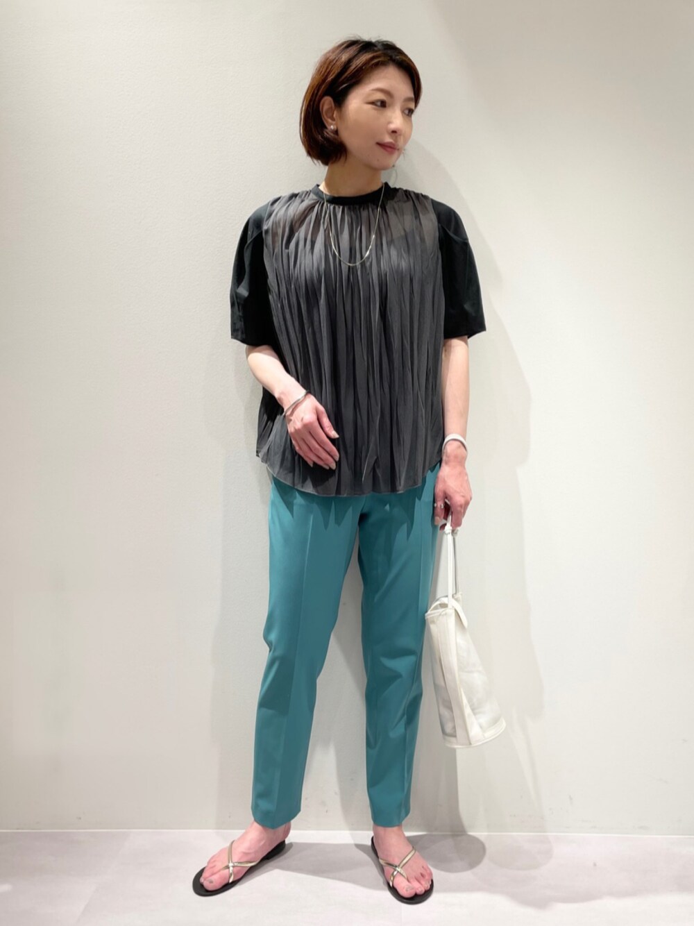 グリーン系のスラックス、グレー系のTシャツ/カットソー、ゴールド系のネックレスを着用したレディースの春コーディネートの1枚目の写真