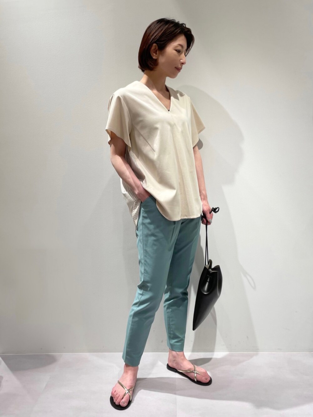 グリーン系のスラックス、ベージュ系のTシャツ/カットソー、ゴールド系のサンダルを着用したレディースの夏コーディネートの1枚目の写真