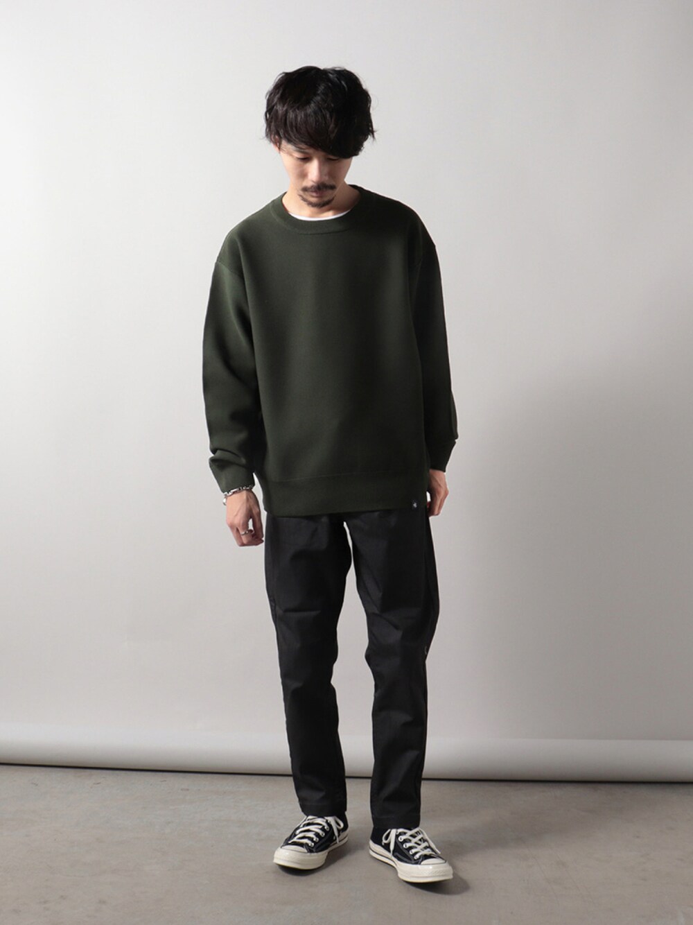 グリーン系のニット/セーター、グレー系のチノパンツ、ブラック系のスニーカーを着用したメンズの秋コーディネートの1枚目の写真