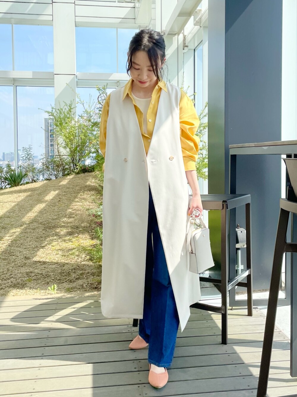 ブルー系のデニムパンツ、オレンジ系のパンプス、ベージュ系のベストを着用したレディースの春コーディネートの1枚目の写真