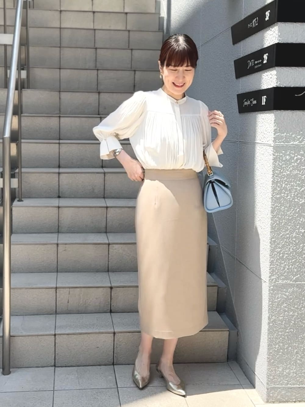 ブルー系のショルダーバッグ、ゴールド系のパンプス、ベージュ系のスカートを着用したレディースの春コーディネートの1枚目の写真