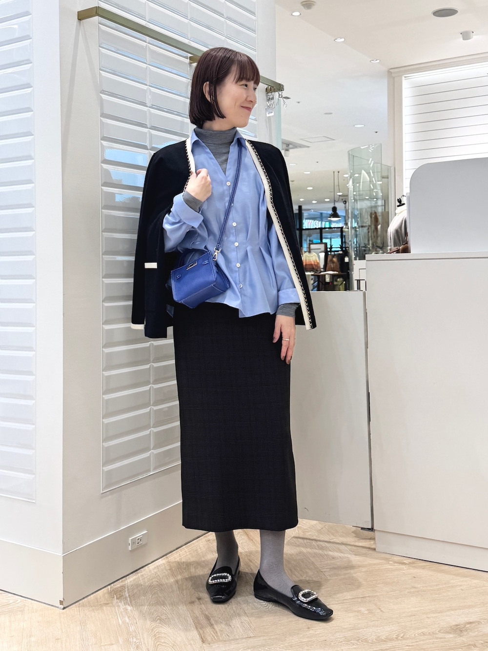 グレー系のニット/セーター、ベージュ系のスカート、ブルー系のショルダーバッグを着用したレディースの秋コーディネートの1枚目の写真